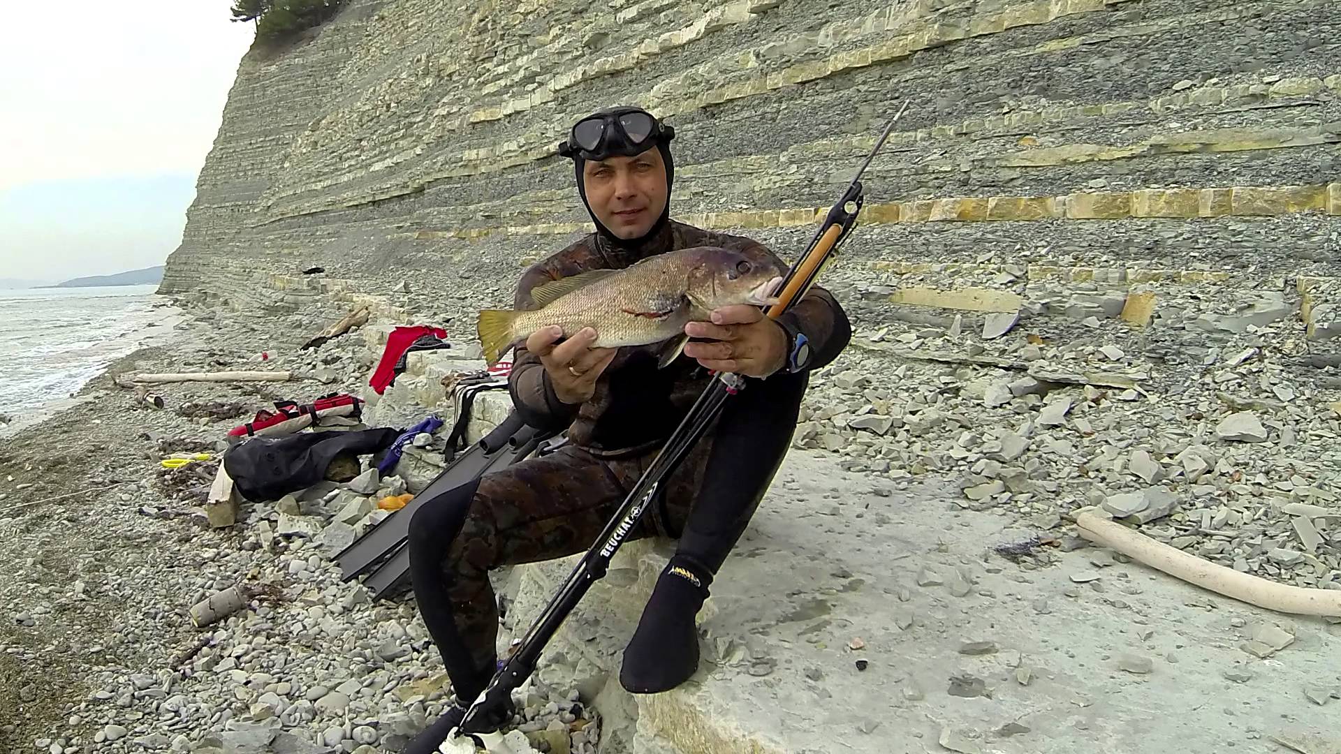 Парень в гидро костюме с рыбой в руках 