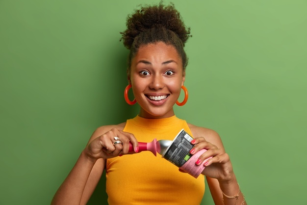 Самое свежее мороженое на земле. счастливая улыбающаяся темнокожая женщина любит есть замороженный десерт в жаркую погоду, у нее белоснежные зубы, хорошее настроение, она носит желтую футболку, изолированную на зеленой стене