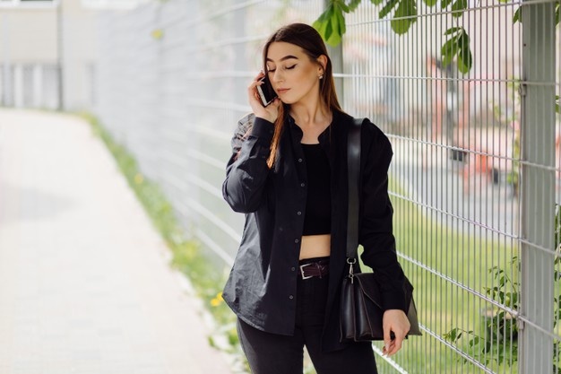 Веселая красивая брюнетка женщина в хорошем настроении пользуется телефоном на улице